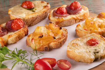 collection of bruschetta baked in slices of bread with melted cheese, cherry tomatoes in cattail on wooden table close-up