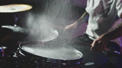 The drummer hits the wet drum cymbal with his drumstick and the water splashes in slow motion. In the recording studio of musical instruments