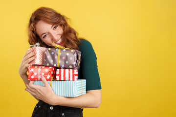 Redheaded woman embracing many gifts while smiling at camera