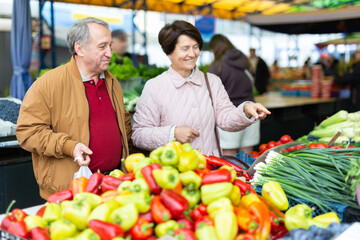 Aged man and woman customers buying vegetables in open-air market