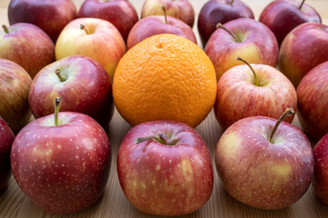 One orange among red apples