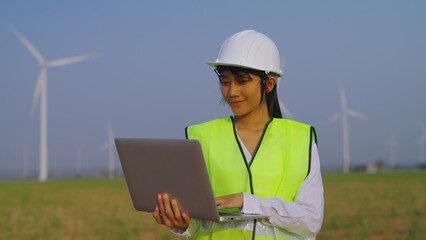 Female engineer using laptop at wind turbine farm. She searching data and working at wind turbine farm. examining wind turbines