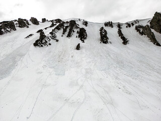 A snowy mountain with ski tracks on it and a cloudy sky in the background.