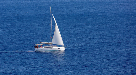 Sailboat with white sail in blue Aegean sea background. Summer holiday in Greece, Cyclades island.