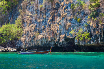 Naklejka na ściany i meble Old traditional Thai motorboat made of wood for fishing and tourists on excursions in the Andaman Sea near Phi Phi Leh island in clear turquoise water under a blue sky. Travel and vacation in phuket.