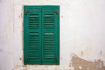 Fototapeta na wymiar Old fashioned closed green wooden shutter on peeled white wall background. Cyclades Greece. Space