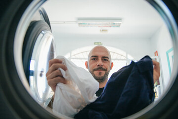 A man loads the washing machine with dirty clothes in the laundromat
