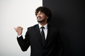 Happy Indian businessman pointing away while standing against black and white background