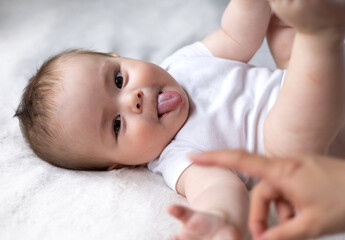 baby lying on bed holding feet with small hands, tongue out smiling profile side view.toddler...