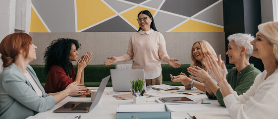 Group of happy mature women applauding while having business meeting in the office