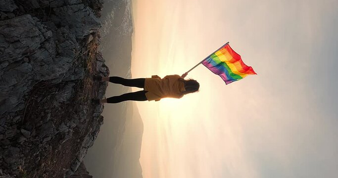 LGBTQ community. A symbolic moment of a woman standing at the top of the mountain and waving rainbow flag. Celebration of diversity, equality and inclusivity