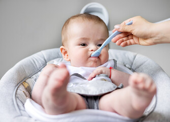 adorable cute baby boy sitting in swing cradle eating mashed food with spoon.mother hand feeding...