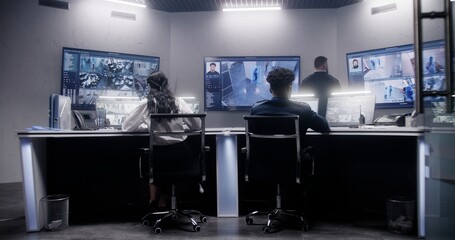 Multi ethnic team of security officers work in surveillance room. Multiple big screens on the wall with displayed security cameras view. Tracking and monitoring systems. Concept of social safety.