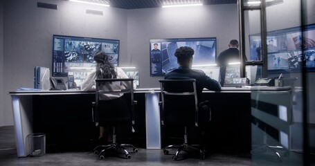 Multi ethnic team of security officers work in surveillance room. Multiple big screens on the wall with displayed security cameras view. Tracking and monitoring systems. Concept of social safety.