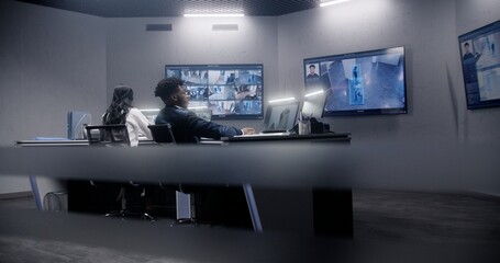 Multi ethnic team of security officers work in surveillance room. Multiple big screens on the wall with displayed security cameras view. Tracking and monitoring systems. Concept of social safety.