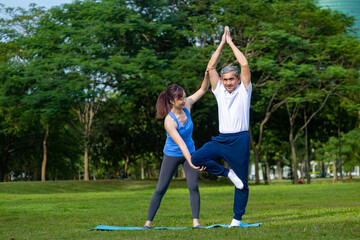 Senior asian man is practicing balance yoga in one leg standing while his daughter is supporting at the public park for elder longevity exercise and outdoor workout usage