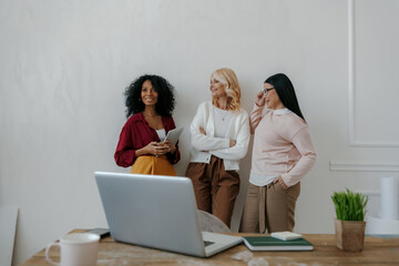 Three mature women communicating and smiling while leaning on the wall in office
