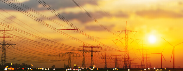 industrial landscape with power lines, high voltage towers and wind turbines on sunset sky...