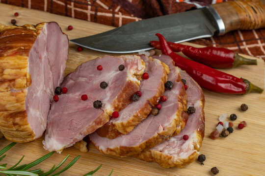 Slices of juicy and delicious pork bacon on a wooden cutting board with a carving knife, multi-colored allspice peas, red hot peppers, parsley, dill and basil. The concept of meat products