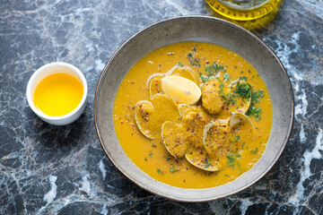 Plate of cream-soup with chickpeas and vongole clams on a black marble background, horizontal shot, selective focus