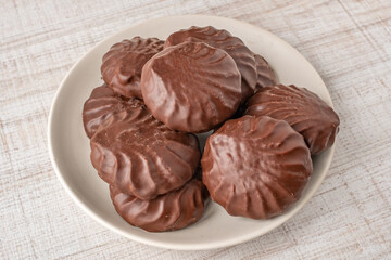 Zephyr in chocolate glaze in a beige cup. Close-up of chocolate marshmallows in a brown bowl on a light table. The concept of confectionery sweets