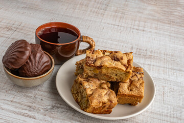 Black tea in a cup, apple pie in a bowl and marshmallows in chocolate glaze in a bowl. Close-up of dessert for tea drinking. The concept of drinking tea at home in a family environment