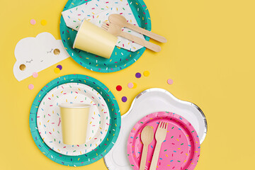 Cute paper party plates and cups for themed kids party on yellow background. Birthday party decorations and props in bright colors. Set of holiday disposable tableware for party or picnic. - obrazy, fototapety, plakaty