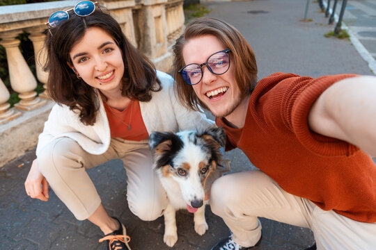 Happy young Caucasian couple with purebreed aussie dog take selfie photo. City life. Training pet