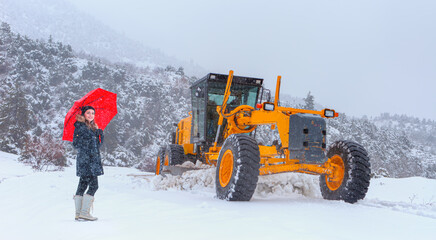 The bulldozer cleans snow on the  road, with snowstorm in the background - Beautiful girl in black...