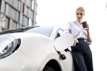 Progressive businesswoman with electric car and charging station before driving around city center....