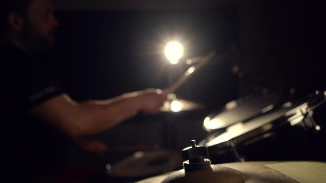 Bearded man brummer musician is playing on drum kit in the dark, side view.