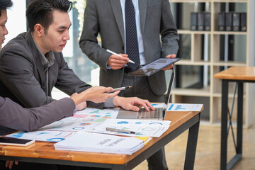 Asian business team consists of marketing staff. accountant and financial officer Help each other analyze company profits using tablets. calculator Laptop computers, graph paper, and corporate pens.