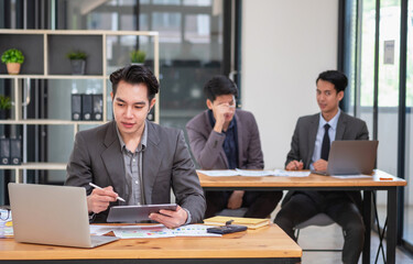 Asian business team consists of marketing staff. accountant and financial officer Help each other analyze company profits using tablets. calculator Laptop computers, graph paper, and corporate pens.