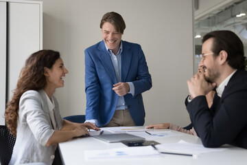 Happy diverse employees laugh at briefing in boardroom, analyzing statistics, take break from financial report, have fun, tell jokes, enjoy conversation, work moments. Teamwork, success in business