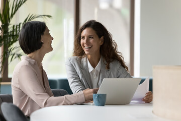 Two happy businesswomen, office employees work in office, laughing, joking during workflow, share creative ideas, solution feel satisfied with corporation, engaged in teamwork. Negotiation, business