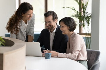 Diverse business team discuss project using modern laptop in office, share good news, show new app, enjoy workflow together, give advice to workmates and help with computer work, prepare joint plan