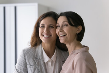 Beautiful mature Caucasian and young Hispanic businesswomen colleagues in elegant formal wear staring aside smiling posing indoors, feel happy, photoshoot for corporate album. Friendship at workplace