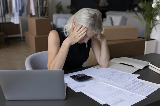 Mature business woman counting expenses, too high rental fees, taxes at workplace, checking invoices, paying bills, counting small budget in storage, warehouse, finding bad financial problems, failure
