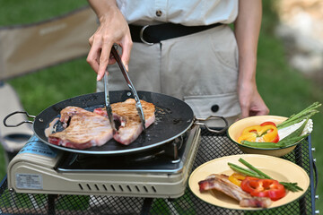 Close up and cropped with female grilling steak on pan with picnic gas stove.