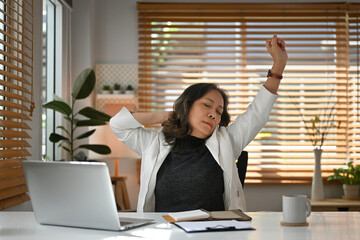 Senior Mature Businesswoman stretching arms on herself due to working with laptop computer.