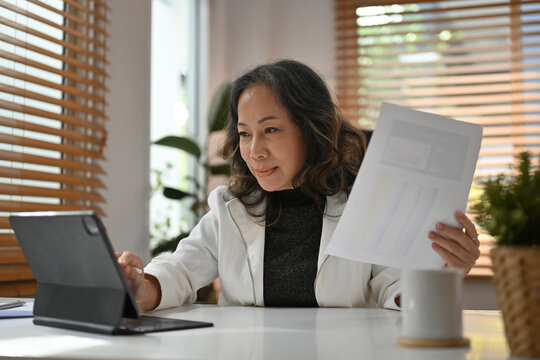 Senior Business woman working with digital tablet and financial document at the office desk.