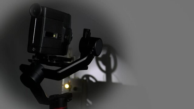 An old movie camera works on an automatic steadicam against the background of a movie projector.