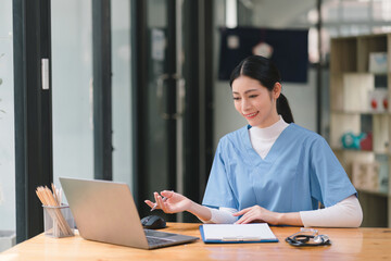Fototapeta premium A confident,Beautiful, professional, millennial female doctor or nurse is working online with a laptop while sitting at a desk in a hospital consultation room.