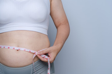 Close-up shot of a fat woman taking a tape measure around her waist Excess fat on her belly, weight gain. Health care concept.