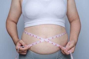 Fat woman in white tank top measures her waist with a tape measure, Excess belly fat, overweight, tummy, dieting concept, want to lose weight