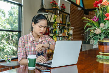 Asian businesswoman looking serious looking at wrist watch frustrated with a video call from a customer who is not on time or stressed with work, the unhappy woman checking time anxiety.