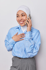 Vertical shot of cheerful businesswoman has pleasant conversation giggles happily keeps smartphone near ear dressed in formal clothing smiles pleasantly looks aside isolated over white background