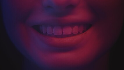 A young attractive girl smiles with her teeth. Sexy smile in neon light, red and blue color. A beautiful woman flirts with her mouth