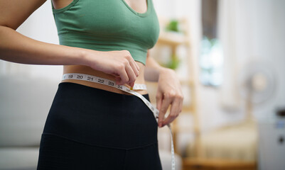 Asian healthy woman dieting Weight loss. Slim woman measuring waist with measure tape after diet at home weight control.