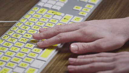 Close-up of a computer keyboard with braille. A blind girl is typing words on the buttons with her hands. Technological device for visually impaired people - obrazy, fototapety, plakaty